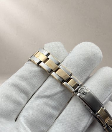 Dettaglio del bracciale rivettato bicolore e della chiusura del Rolex Oyster Perpetual 6619 appoggiati sul guanto bianco.
