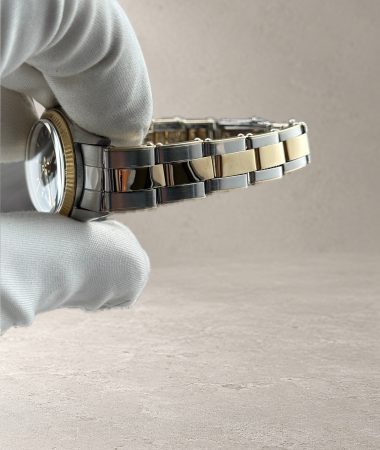 Vista laterale delle maglie rivettate del bracciale bicolore del Rolex Oyster Perpetual 6619, sostenuto tra le dita guantate.