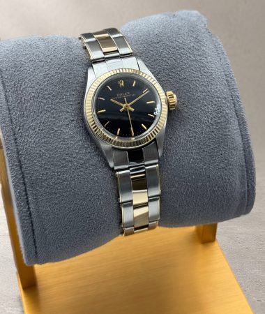 Vista inclinata del Rolex Oyster Perpetual 6619 sul cuscino grigio con base dorata, con quadrante nero e bracciale bicolore.