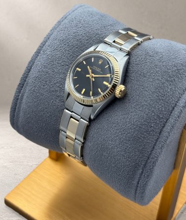 Rolex Oyster Perpetual 6619 a tre quarti sul supporto grigio, con quadrante nero, lunetta scanalata e corona visibili.